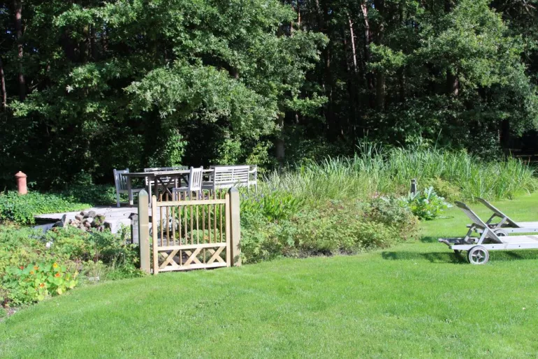 Un portail en bois au milieu d'un jardin verdoyant et une table et des chaises en bois derrière.