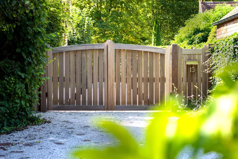 Un portail pivotant en bois avec une arche à côté d'une porte avec le même design et avec un numéro de maison et une boîte aux lettres intégrés.