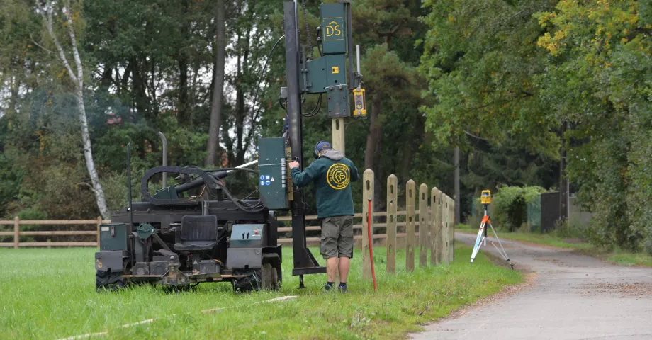 Un homme installe des clôtures en bois à l'aide d'une machine à vibrer les poteaux.