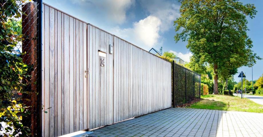 Un portail coulissant en bois pour les propriétés résidentielles avec des planches verticales à côté d'une porte avec un système d'interphone
